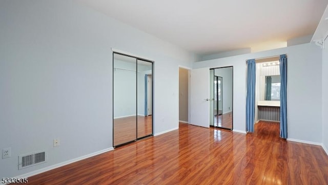 unfurnished bedroom with multiple closets and hardwood / wood-style floors