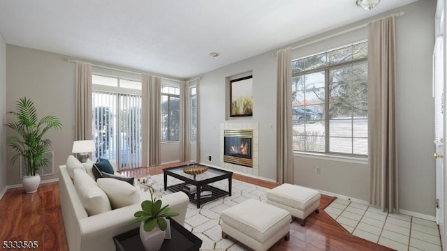 living room featuring a tiled fireplace, a healthy amount of sunlight, and light wood-type flooring