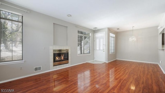 unfurnished living room featuring hardwood / wood-style floors, a tile fireplace, and a chandelier