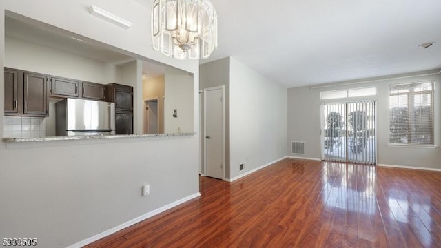 kitchen featuring an inviting chandelier, dark brown cabinetry, light stone countertops, and stainless steel refrigerator