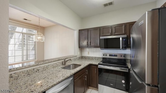 kitchen featuring light stone countertops, appliances with stainless steel finishes, decorative light fixtures, decorative backsplash, and sink