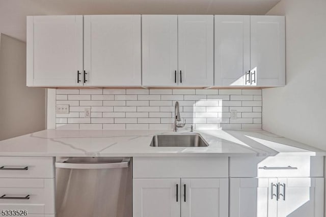 kitchen featuring tasteful backsplash, stainless steel dishwasher, sink, white cabinetry, and light stone counters