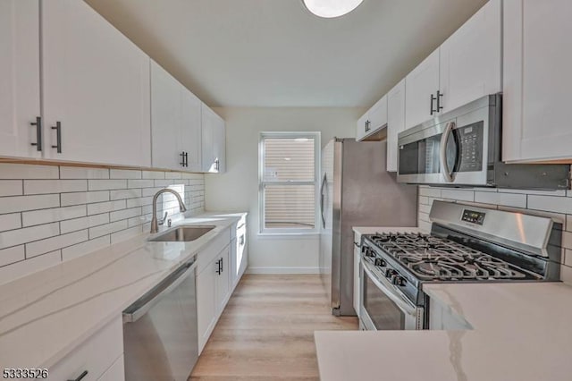 kitchen with light stone countertops, white cabinets, stainless steel appliances, tasteful backsplash, and sink