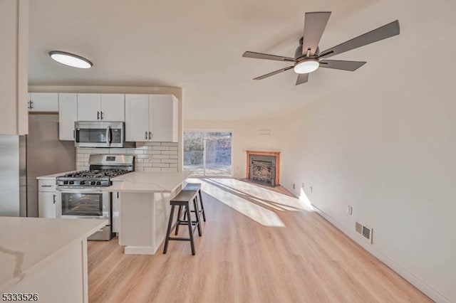 kitchen with white cabinetry, stainless steel appliances, decorative backsplash, a kitchen breakfast bar, and light hardwood / wood-style flooring