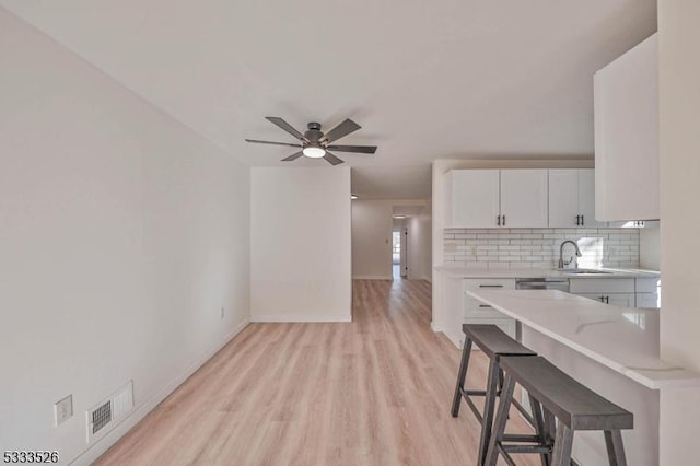 kitchen with white cabinets, tasteful backsplash, a kitchen breakfast bar, ceiling fan, and light hardwood / wood-style flooring