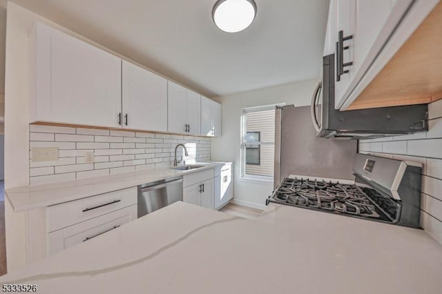 kitchen featuring white cabinetry, stainless steel appliances, backsplash, light stone counters, and sink