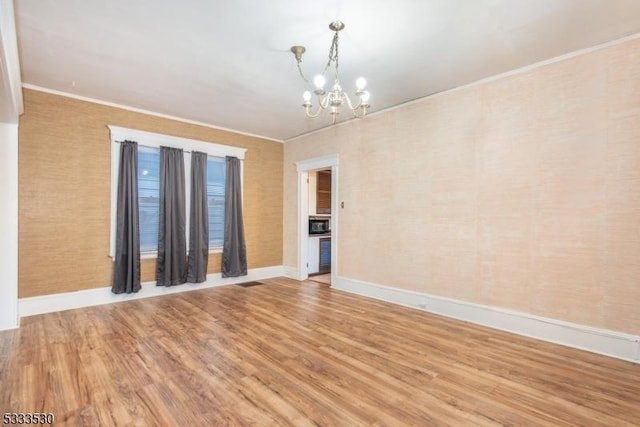 empty room with ornamental molding, hardwood / wood-style flooring, and a notable chandelier