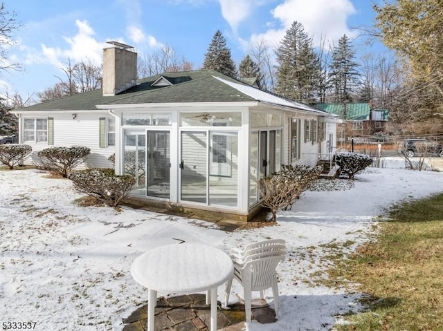 snow covered rear of property with a sunroom