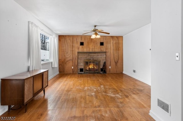 unfurnished living room with ceiling fan, light wood-type flooring, a fireplace, and wood walls