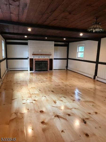 interior space with beamed ceiling, a tiled fireplace, a baseboard heating unit, and wooden ceiling