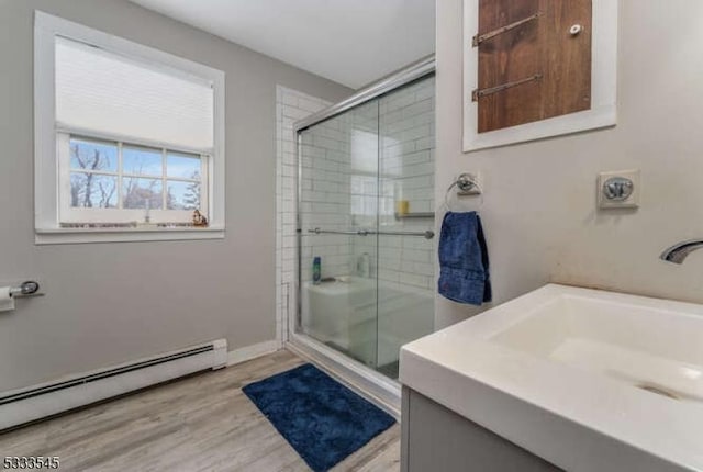 bathroom with vanity, hardwood / wood-style floors, a baseboard radiator, and a shower with shower door