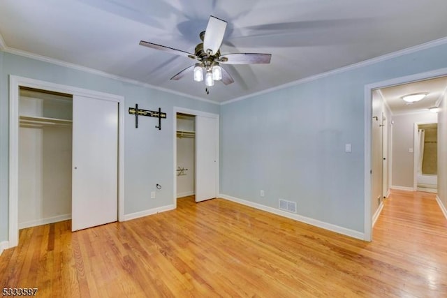 unfurnished bedroom with crown molding, ceiling fan, light wood-type flooring, and two closets