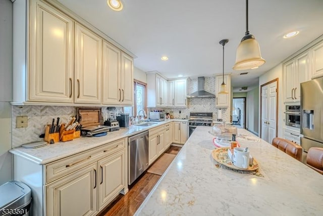 kitchen featuring sink, hanging light fixtures, stainless steel appliances, light stone countertops, and wall chimney exhaust hood