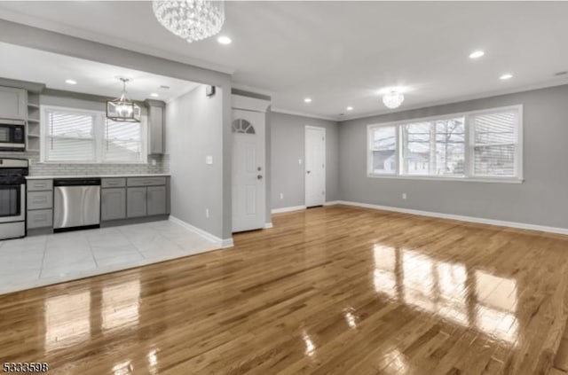 unfurnished living room featuring light hardwood / wood-style flooring, plenty of natural light, ornamental molding, and a chandelier