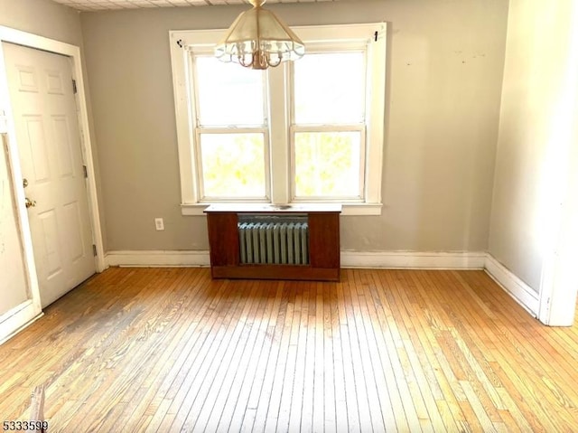 interior space featuring light wood-type flooring, an inviting chandelier, and radiator heating unit