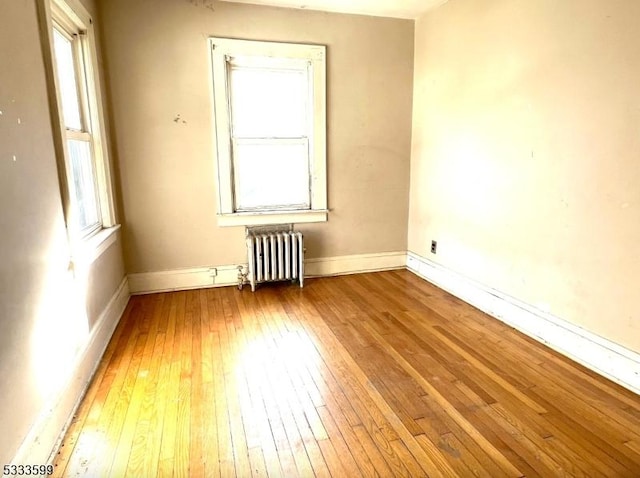 spare room featuring a wealth of natural light, radiator heating unit, and hardwood / wood-style floors