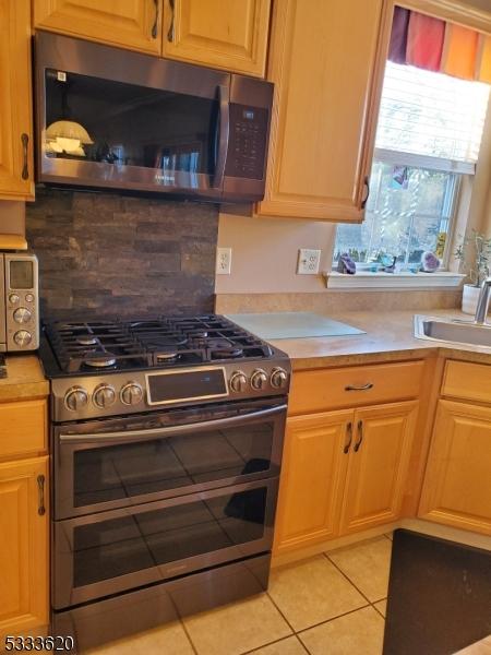 kitchen featuring light tile patterned floors, appliances with stainless steel finishes, decorative backsplash, and sink