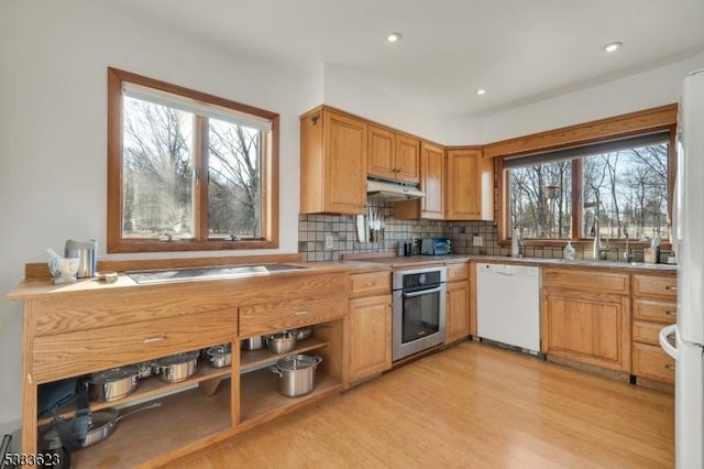 kitchen with tasteful backsplash, under cabinet range hood, light wood-type flooring, light countertops, and white appliances