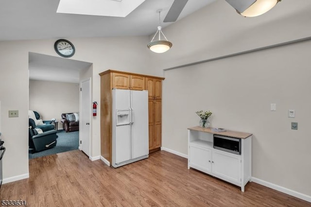 kitchen with lofted ceiling with skylight, white fridge with ice dispenser, baseboards, and light wood-style floors