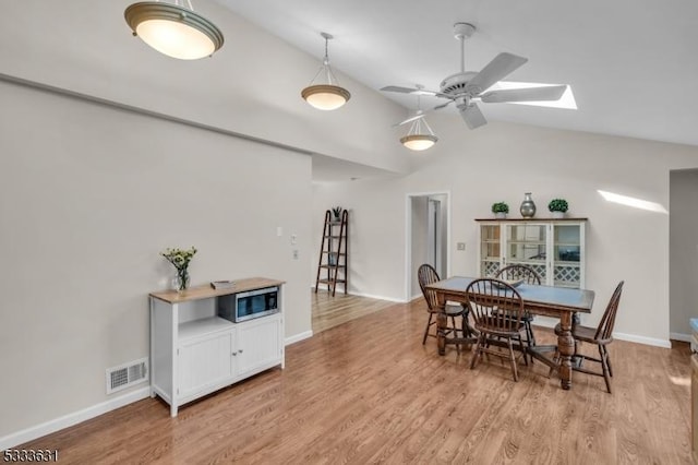 dining area featuring light wood finished floors, visible vents, lofted ceiling with skylight, a ceiling fan, and baseboards