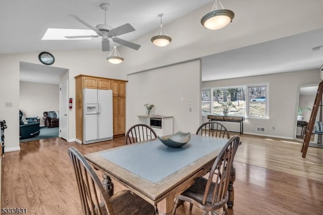 dining room with vaulted ceiling with skylight, visible vents, light wood-style flooring, and baseboards