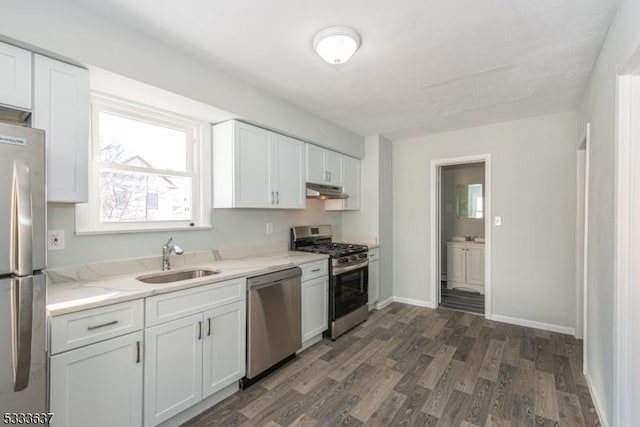 kitchen featuring appliances with stainless steel finishes, sink, white cabinets, dark hardwood / wood-style flooring, and light stone counters