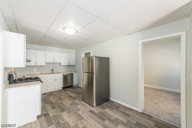 kitchen with appliances with stainless steel finishes, sink, white cabinets, a paneled ceiling, and dark hardwood / wood-style floors