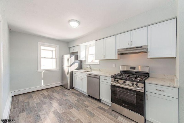 kitchen featuring light stone countertops, baseboard heating, white cabinets, appliances with stainless steel finishes, and light hardwood / wood-style flooring