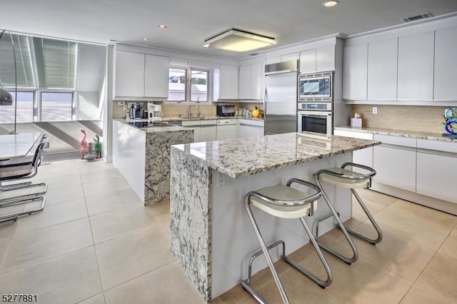 kitchen featuring built in appliances, light tile patterned floors, white cabinets, and a kitchen island