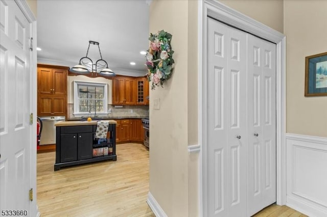 kitchen featuring backsplash, high end stainless steel range, ornamental molding, decorative light fixtures, and light wood-type flooring