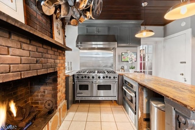 kitchen featuring appliances with stainless steel finishes, pendant lighting, exhaust hood, light tile patterned floors, and a brick fireplace