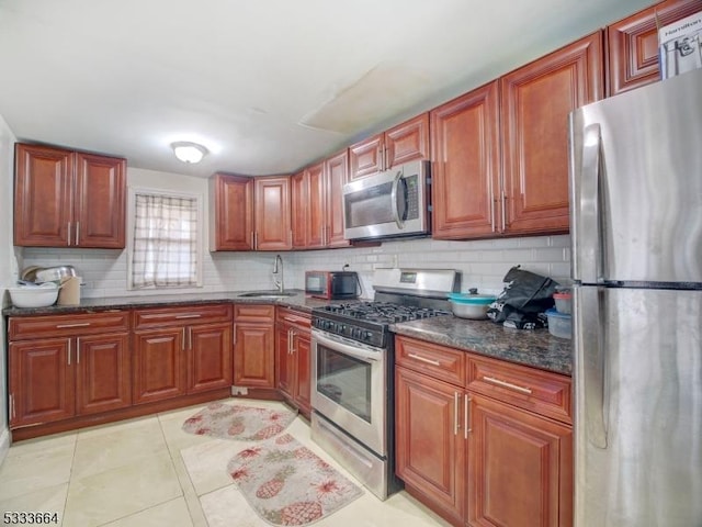 kitchen with backsplash, sink, stainless steel appliances, light tile patterned floors, and dark stone counters