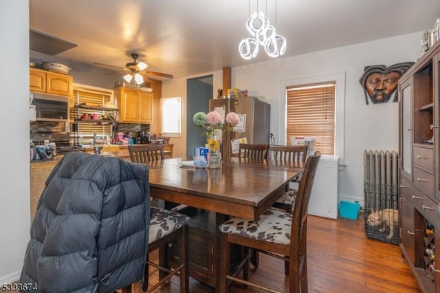 dining area featuring radiator heating unit, ceiling fan with notable chandelier, and dark hardwood / wood-style floors