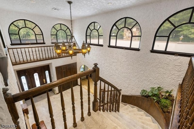 stairway featuring an inviting chandelier, plenty of natural light, carpet flooring, and a textured ceiling