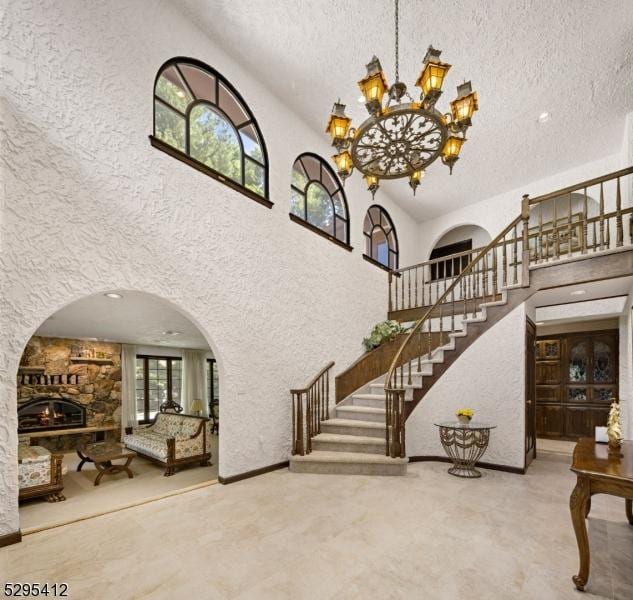 stairway featuring a towering ceiling, a chandelier, a textured ceiling, and a fireplace