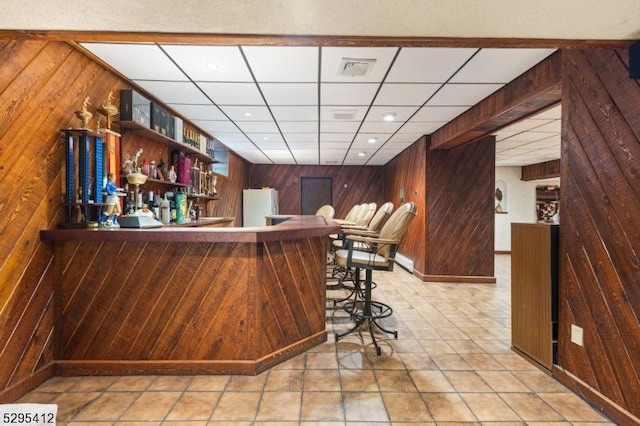 bar featuring a drop ceiling, white fridge, and wood walls