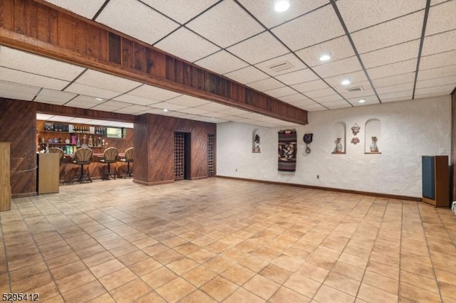 basement with a paneled ceiling, bar area, and wood walls