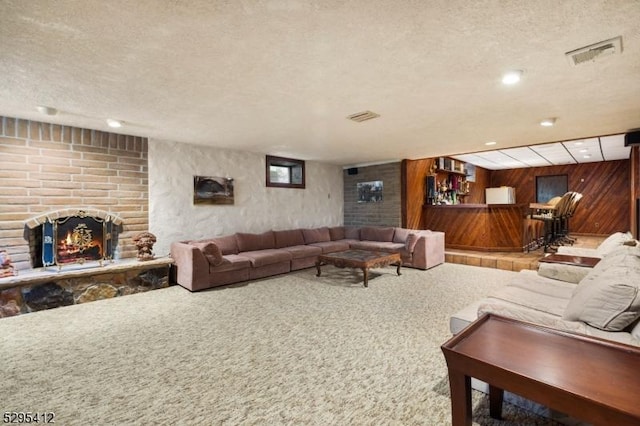 living room with a brick fireplace, wooden walls, a textured ceiling, and carpet flooring