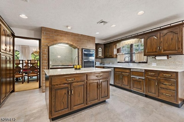 kitchen with a kitchen island, tasteful backsplash, sink, light stone counters, and stainless steel appliances