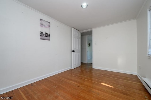 empty room with crown molding, hardwood / wood-style floors, and baseboard heating