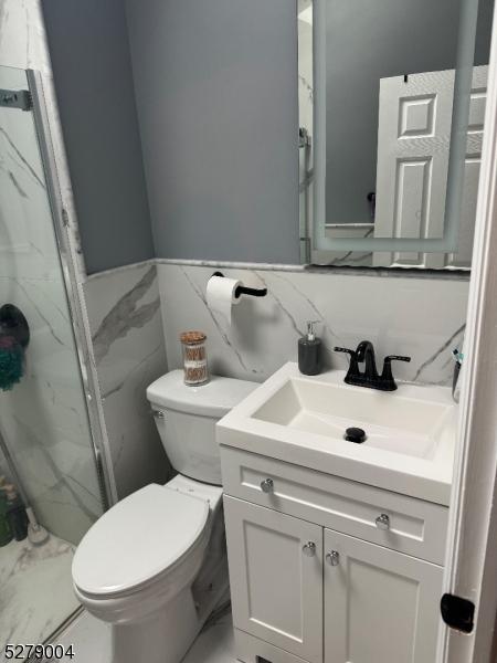 bathroom featuring toilet, tile walls, an enclosed shower, and vanity