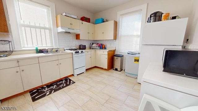 kitchen with cream cabinetry, tasteful backsplash, white appliances, a wealth of natural light, and sink