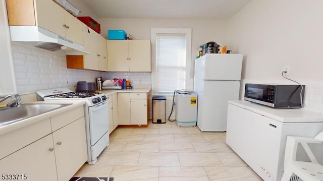 kitchen featuring sink, decorative backsplash, cream cabinets, and white appliances