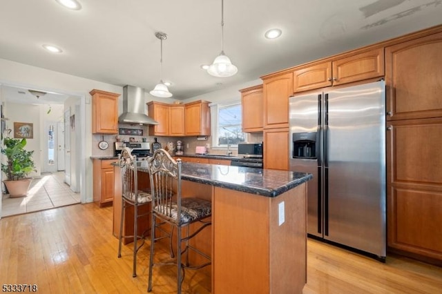 kitchen with wall chimney exhaust hood, dark stone countertops, decorative light fixtures, a center island, and stainless steel appliances