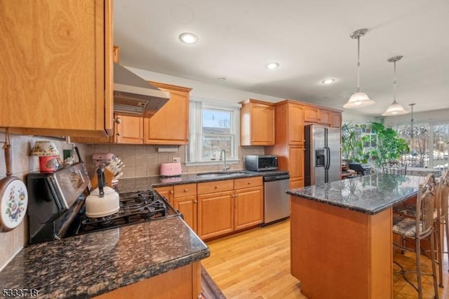 kitchen featuring a center island, decorative light fixtures, appliances with stainless steel finishes, a sink, and wall chimney exhaust hood