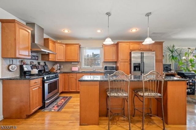 kitchen featuring stainless steel appliances, decorative light fixtures, a kitchen island, and wall chimney range hood