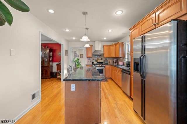 kitchen with a center island, pendant lighting, stainless steel appliances, wall chimney range hood, and light wood-type flooring