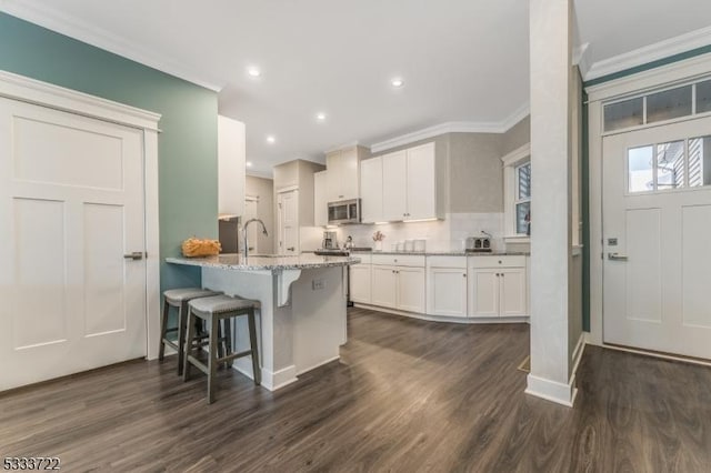 kitchen featuring stainless steel microwave, crown molding, dark wood finished floors, a kitchen breakfast bar, and white cabinets