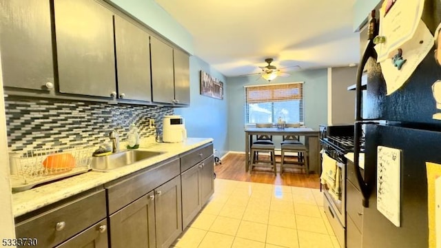 kitchen featuring ceiling fan, sink, stainless steel range with gas cooktop, decorative backsplash, and black fridge