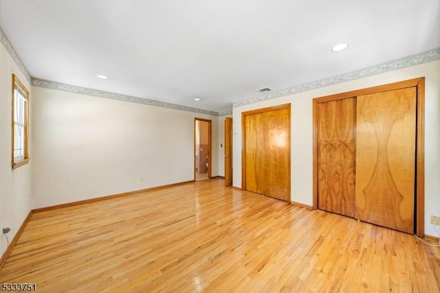 unfurnished bedroom featuring multiple closets and light hardwood / wood-style floors